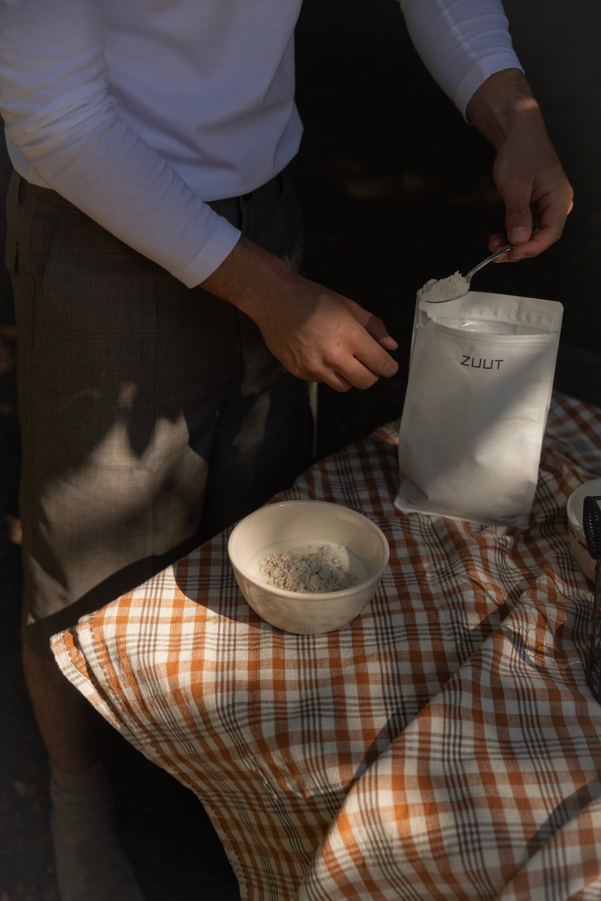 Person scoop organic whey protein in yoghurt outside on a checkered table cloth.