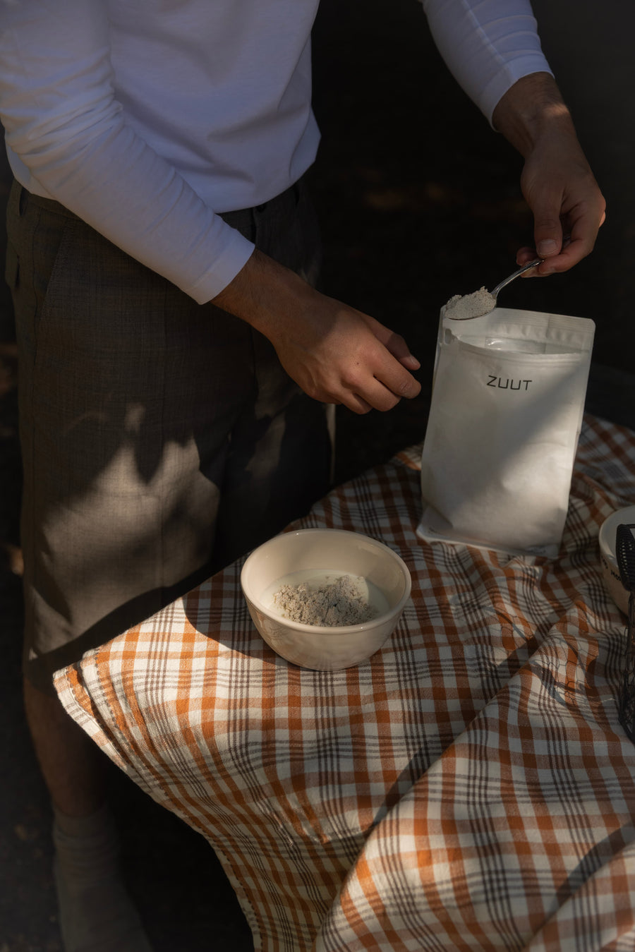 Person scoop organic whey protein in yoghurt outside on a checkered table cloth.